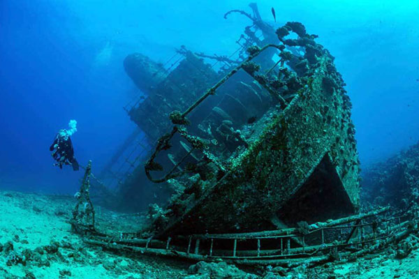 Scuba diver exploring the historic SS Thistlegorm wreck in Egypt’s Red Sea surrounded by vibrant coral and marine life.